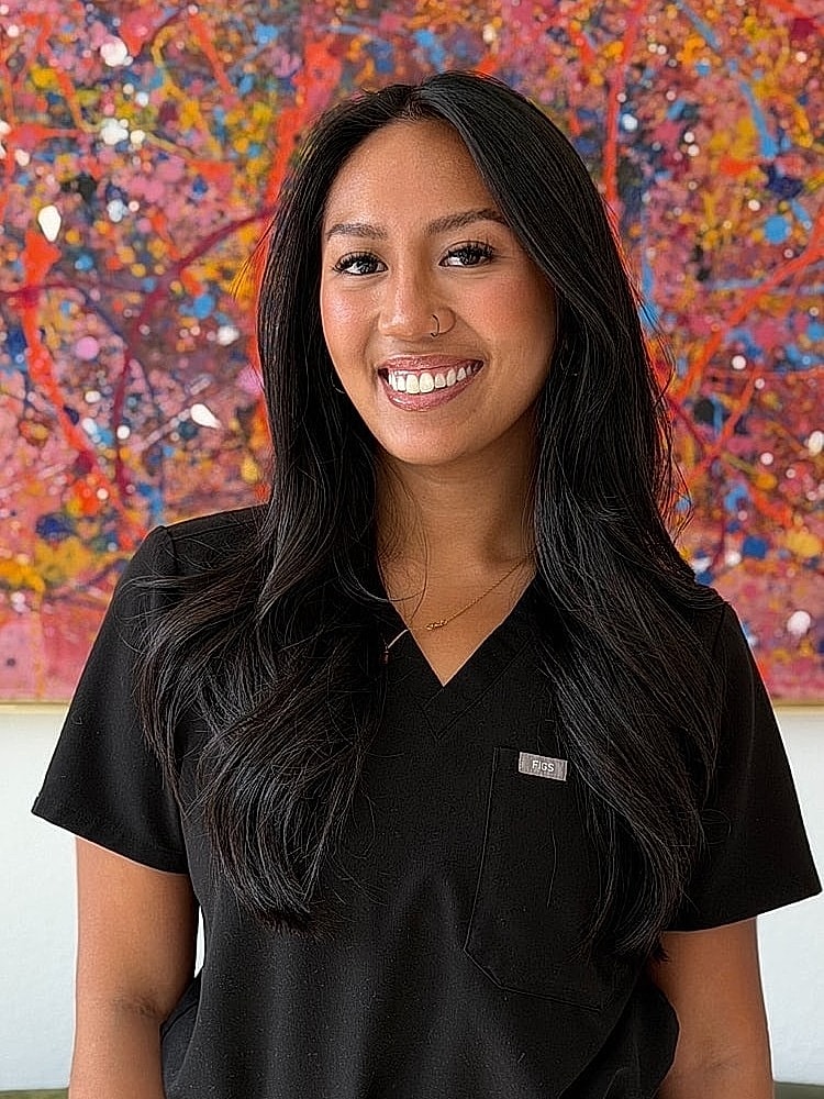 Smiling woman in black scrubs, colorful background.
