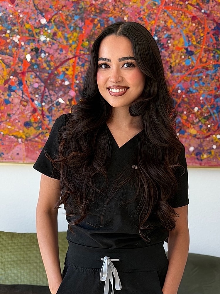 Woman in black scrubs smiling indoors.